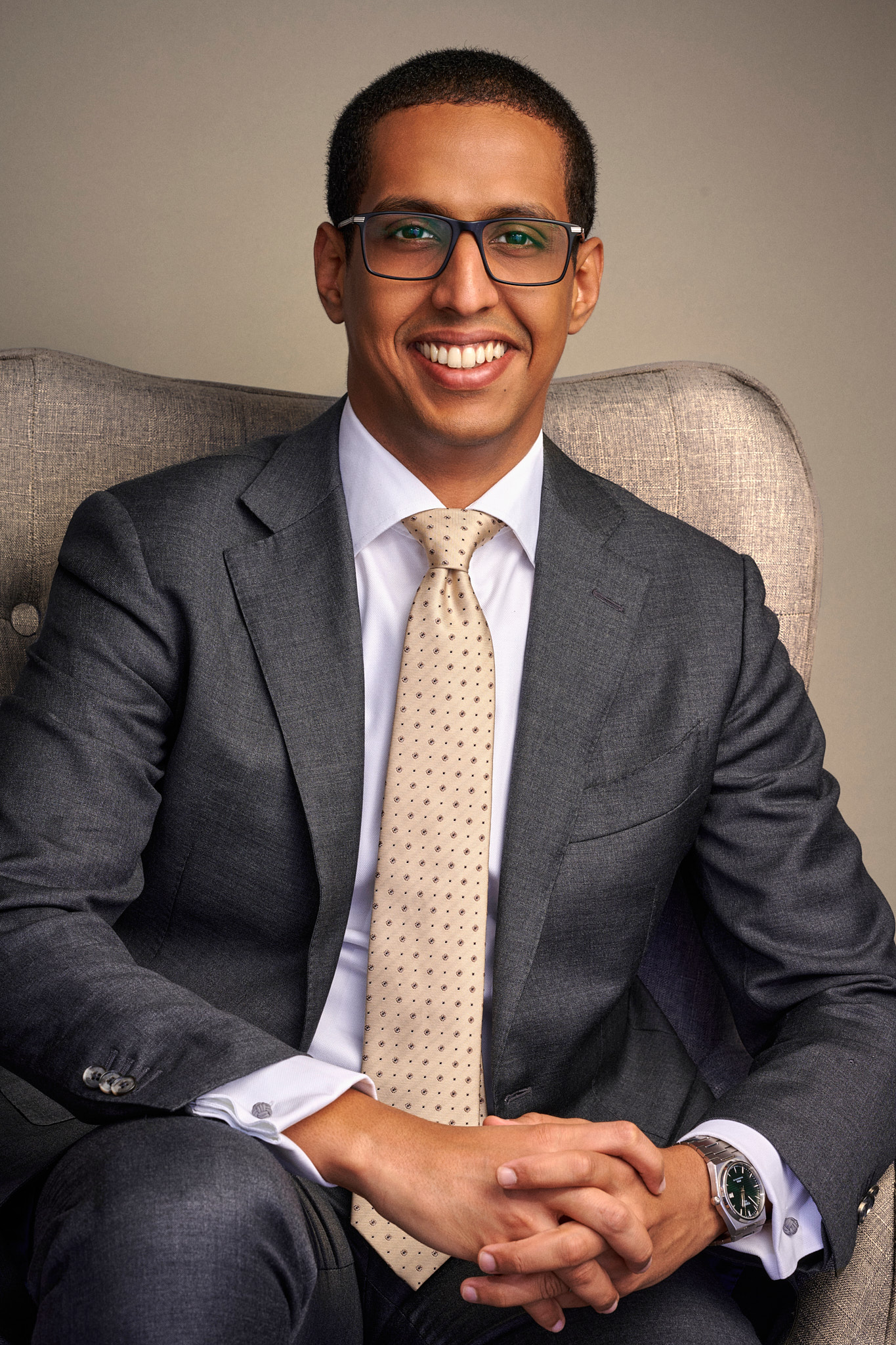 Portrait corporate d'un dirigeant souriant en costume gris et lunettes, assis dans un fauteuil, par Pierre-Yves Queignec, photographe corporate à Paris