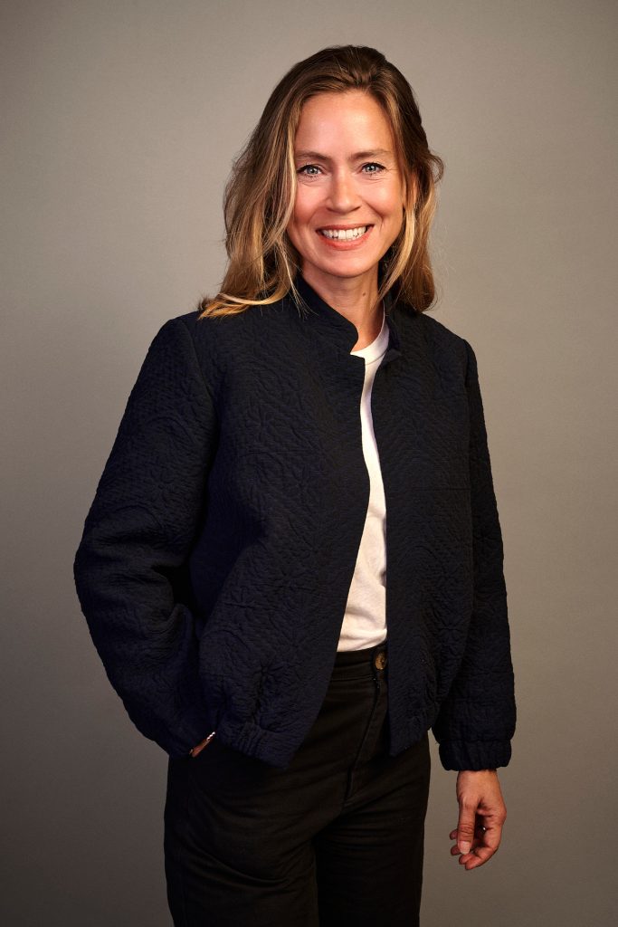 Portrait corporate d'une femme blonde souriante en veste matelassée sombre, par Pierre-Yves Queignec, photographe corporate à Paris.